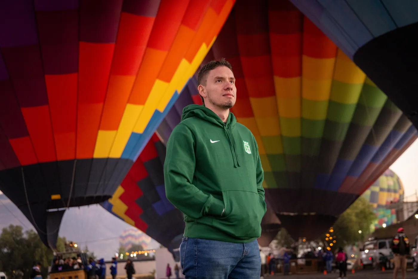 Hombre joven de pie bajo un enorme globo aerostatico de franjas arcoiris antes del despegue