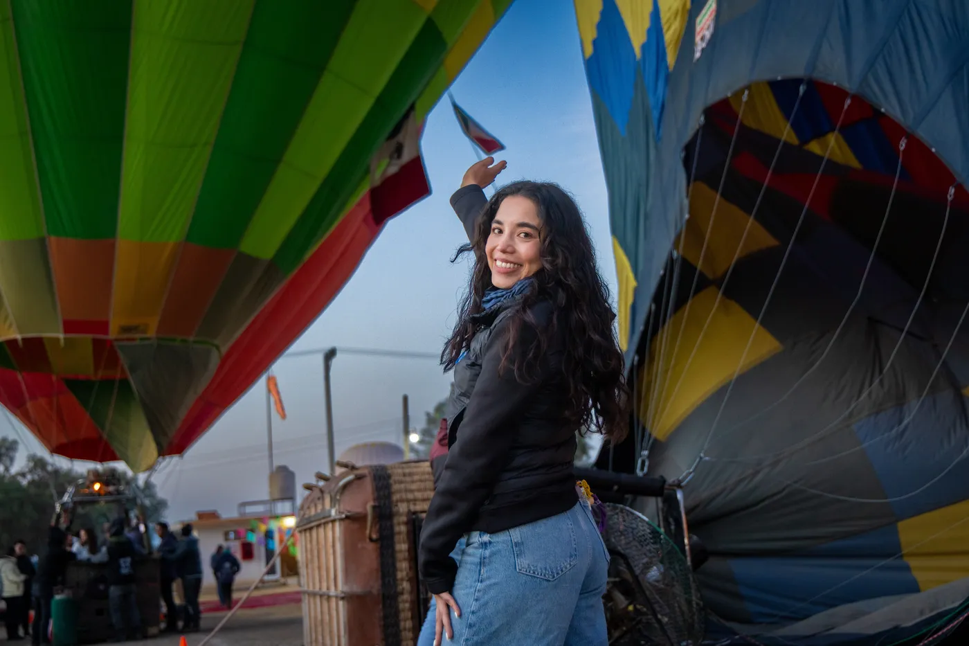 Mujer sonriendo entre globos inflándose al amanecer, vuelo de cumpleaños