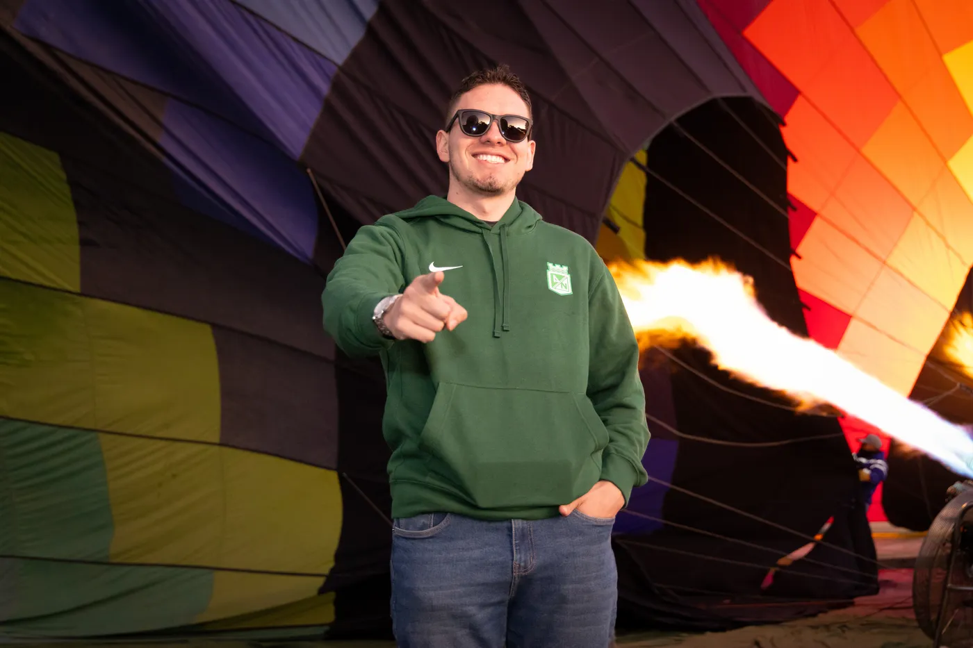 Pasajero con sudadera verde señala a la cámara mientras el quemador infla el globo