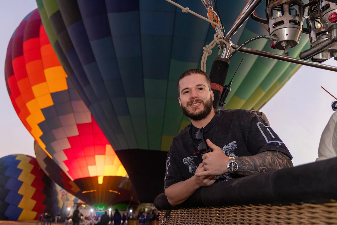 Pasajero sonriente dentro de la canastilla mientras varios globos se inflan e iluminan al amanecer